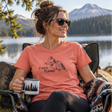 A woman wearing a coral peach short-sleeve T-shirt with a black bird graphic and the words 'FINCH Please' in a natural outdoor setting, plus a close-up of the shirt graphic. The shirt appears to be the product being sold.
